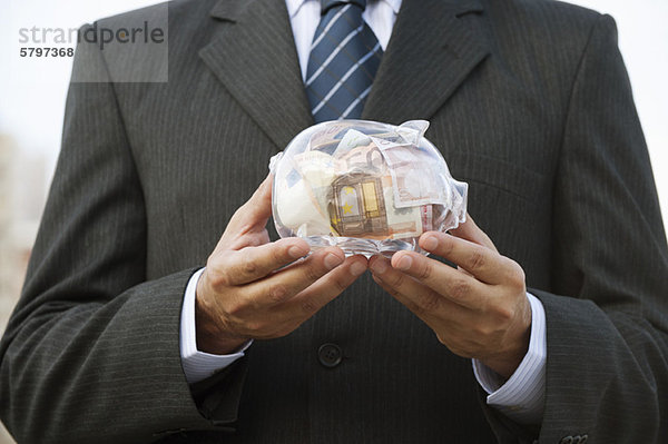 Mann mit transparentem Sparschwein gefüllt mit Euro  beschnitten
