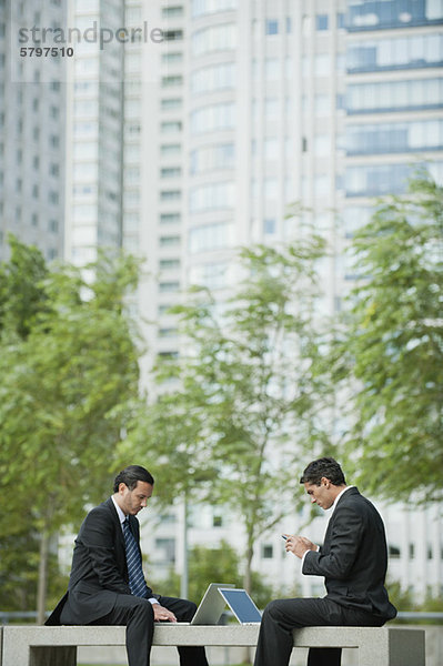 Geschäftsleute sitzen im Freien mit Laptop-Computern  ein Mann Textnachrichten mit Handy