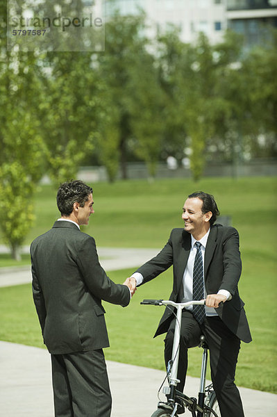 Geschäftsleute begrüßen sich mit Handschlag  ein Mann auf dem Fahrrad