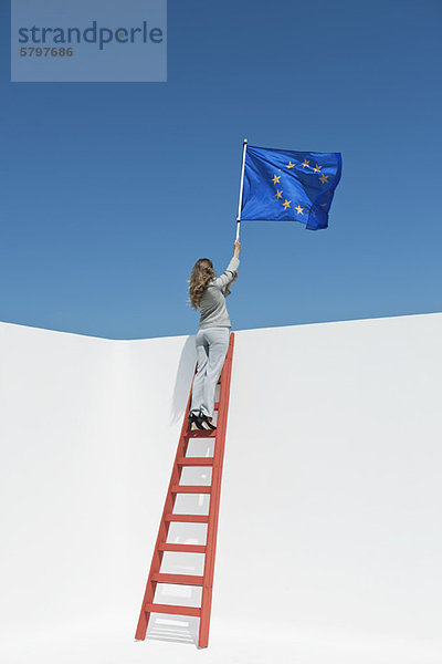 Geschäftsfrau steht oben auf der Leiter und hält die Flagge der Europäischen Union.