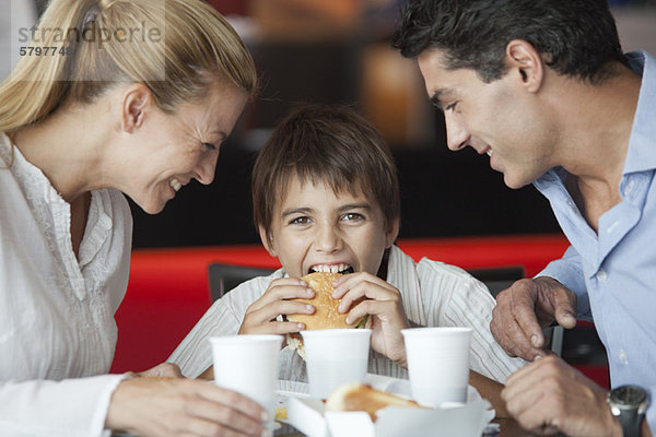 Junge isst Hamburger mit seinen Eltern im Fast-Food-Restaurant