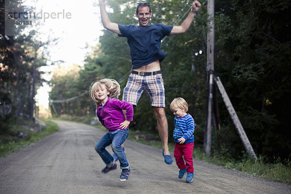 Aufgeregter Vater mit zwei Kindern beim Springen auf der Landstraße
