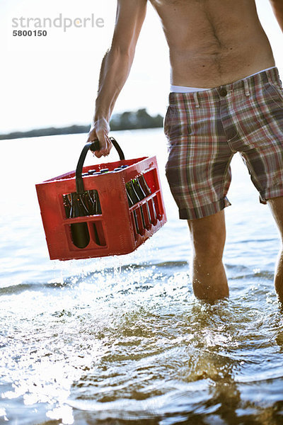 Mittelteil des reifen Mannes mit Getränkekiste im Seewasser