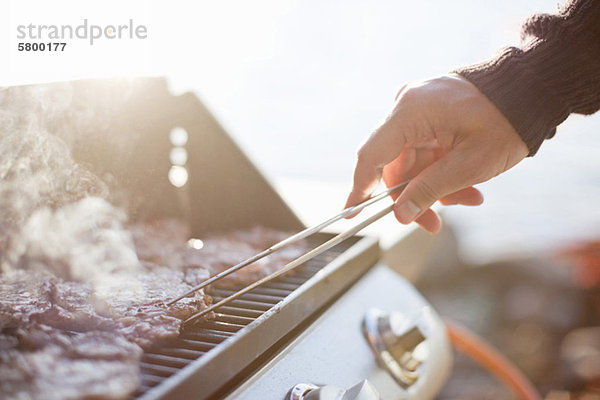 Nahaufnahme eines Mannes  der Rindfleisch mit einer Zange auf dem Grill umdreht.