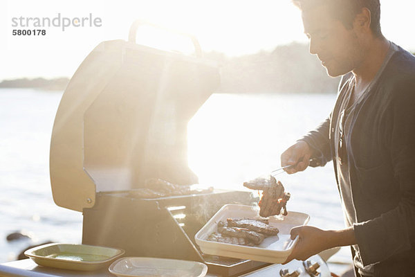 Mann kocht Rindfleisch am See in hellem Sonnenlicht