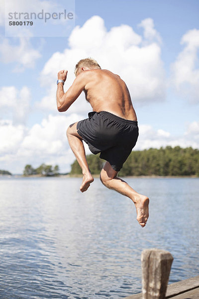 Erwachsener Mann  der an einem sonnigen Tag in den See springt.