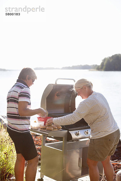 Zwei Personen kochen auf einem Campingkocher in der Nähe des Sees.