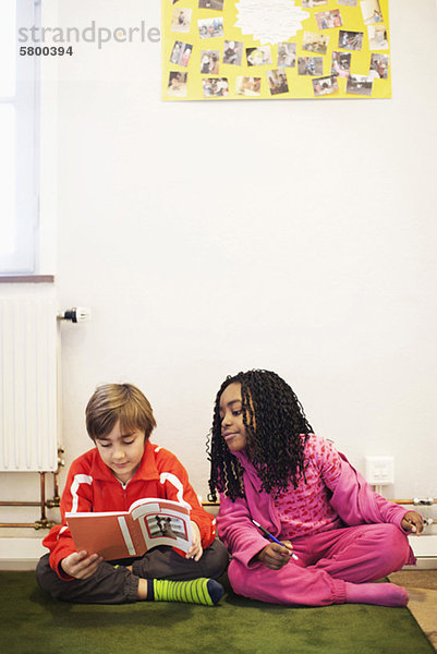 Mädchen und Junge beim Lesen von Büchern auf Teppichen