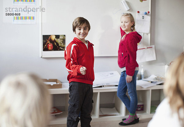 Junge gestikuliert mit Mädchen auf Whiteboard im Klassenzimmer