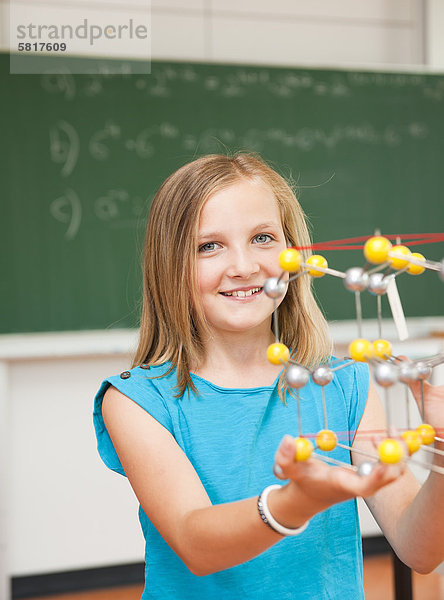 Lächelnde Schülerin hält ein Molekular-Modell im Klassenzimmer  Portrait