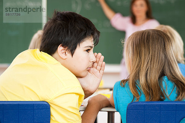 Junge flüstert mit einem Mädchen im Klassenzimmer