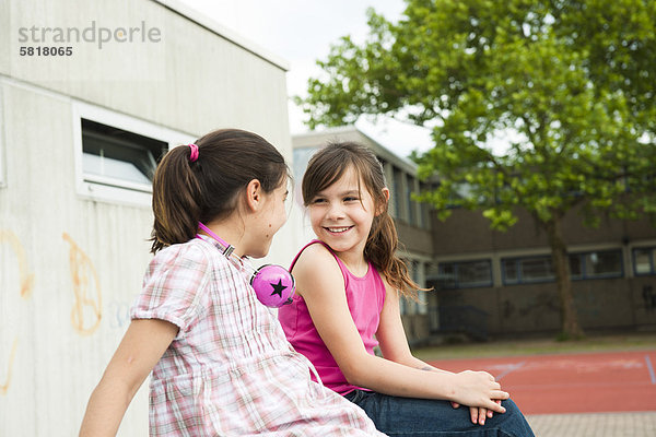 Zwei lächelnde Mädchen sitzen auf dem Schulhof