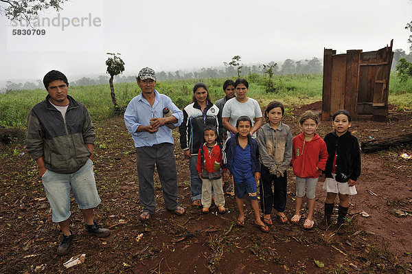 Landgrabbing: Kleinbauernfamilie  die von Investoren von ihrem Land vertrieben wurde und jetzt in einer provisorischen Hütte am Straßenrand lebt  hinten das Sojafeld eines Großgrundbesitzers auf ihrem ehemaligen Land  Landgrabbing  Distrikt Carlos Antonio Lopez  Provinz Itapua  Paraguay  Südamerika