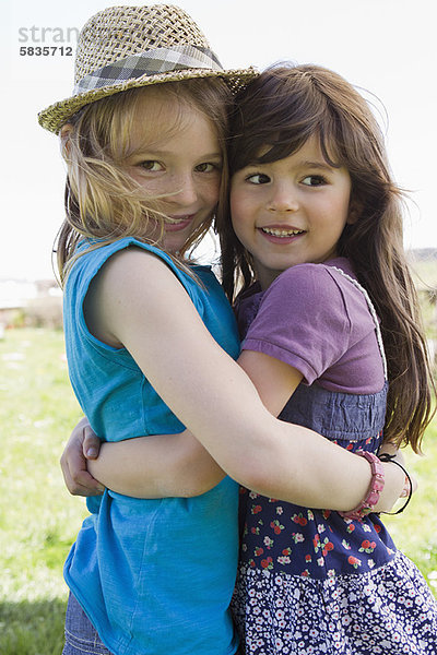 Lächelnde Mädchen  die sich im Freien umarmen.