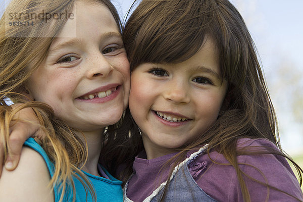 Lächelnde Mädchen  die sich im Freien umarmen.