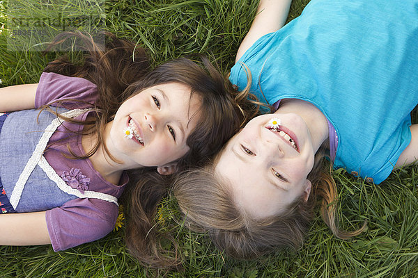 Lächelnde Mädchen  die zusammen im Gras liegen.