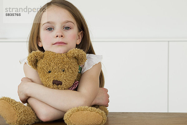 Mädchen umarmender Teddybär am Tisch