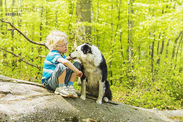 Junge sitzend mit Hund im Wald