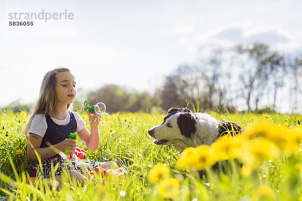 Mädchen bläst Blasen mit Hund im Feld