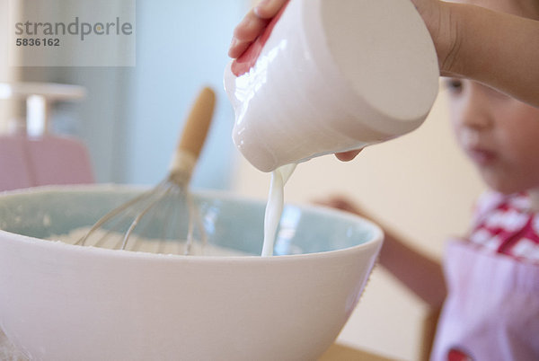 Mädchen gießt Milch in den Teig in der Küche.