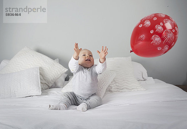 Baby Junge spielt mit Ballon auf dem Bett