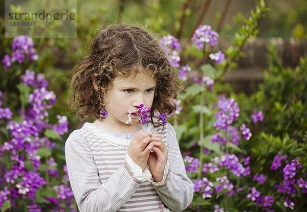 Kleines Mädchen riecht an einer Gartenblume
