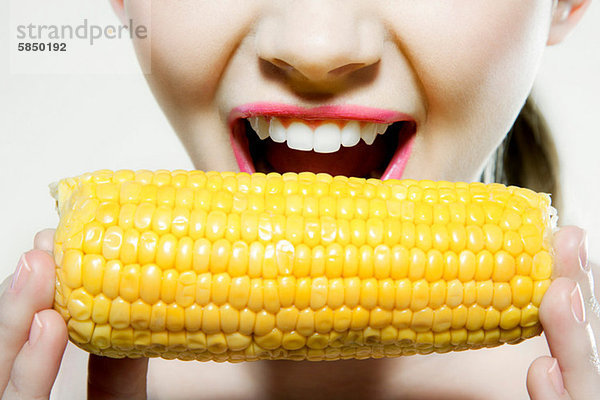 Junge Frau beißt Maiskolben Mund