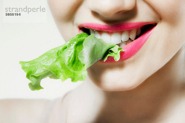 Junge Frau beißt Kopfsalat  Mund