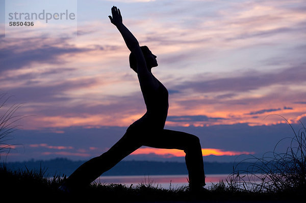 Silhouette der Frau in Krieger-Yoga-Pose bei Sonnenuntergang