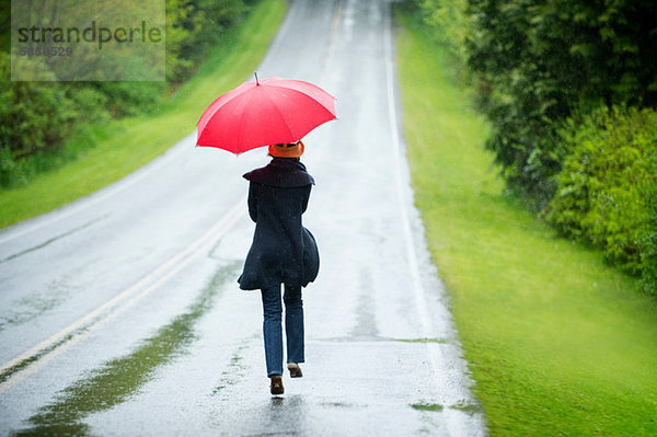 Frau auf leerer Straße mit rotem Regenschirm