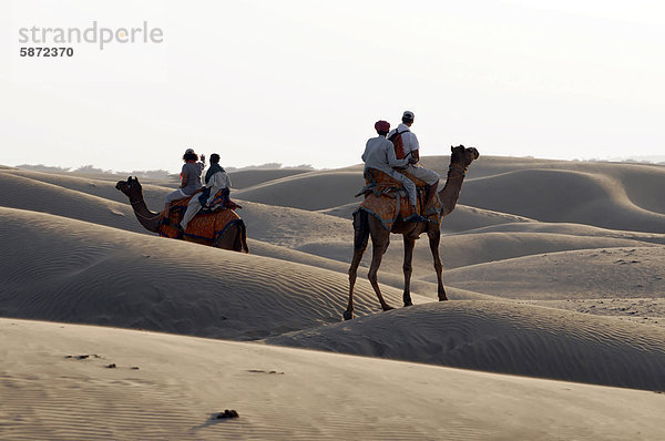 Touristen mit Führern reiten mit Kamelen  Dromedare (Camelus dromedarius) durch die Wüste  Wüste Thar  Rajasthan  Indien  Asien