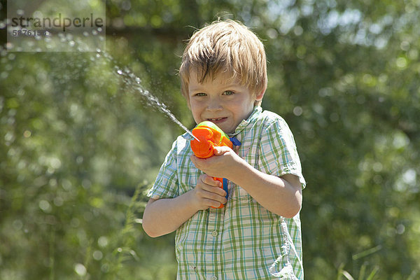 Kleiner Junge spritzt mit einer Wasserpistole