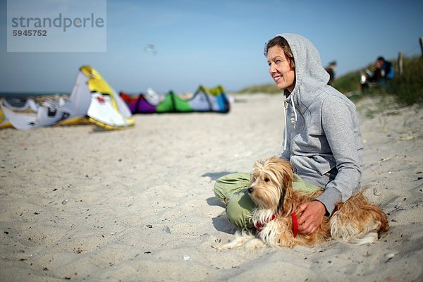Frau sitzt mit Hund am Strand in Fehmarn  Schleswig-Holstein  Deutschland
