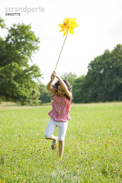 Mädchen läuft mit einem Windrädchen auf einer Wiese
