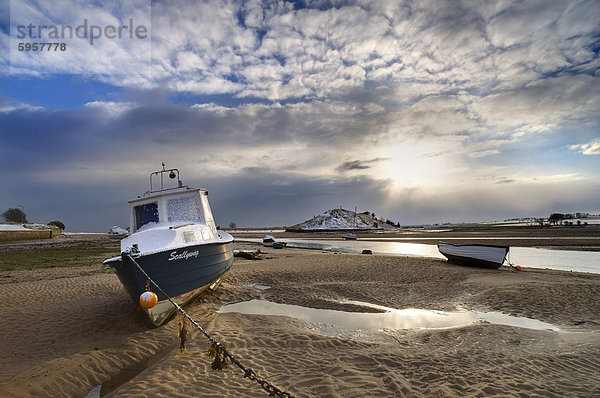 Blick über Aln-Mündung bei Ebbe mit Boot und Distanyt Bereiche  die in Schnee und Sonne durchbrechen Winter Himmel  Northumberland  England  Uninted Königreich  Europa