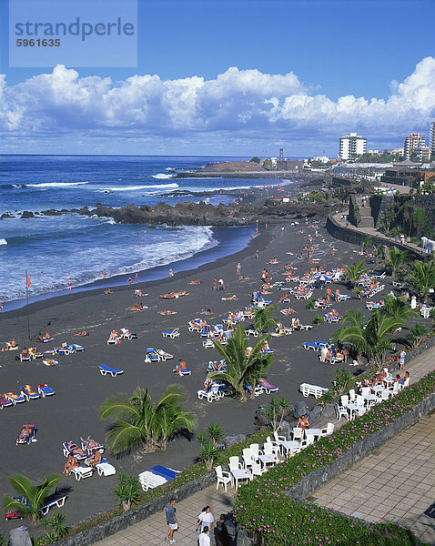 Touristen auf vulkanischen Sandstrand Playa Jardin  mit Burg San Felipe und Hotel Puerto Playa darüber hinaus  bei Puerto De La Cruz  Teneriffa  Kanarische Inseln  Spanien  Atlantik  Europa