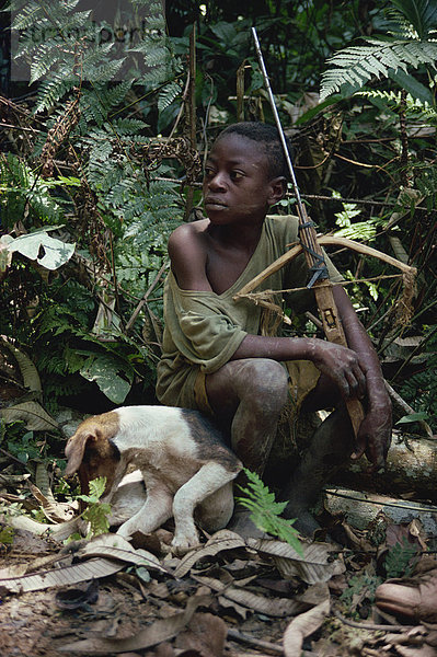 Kleiner Junge sitzt im Dschungel mit Hund und hölzerne Armbrust  Südosten  Kamerun  Westafrika  Afrika