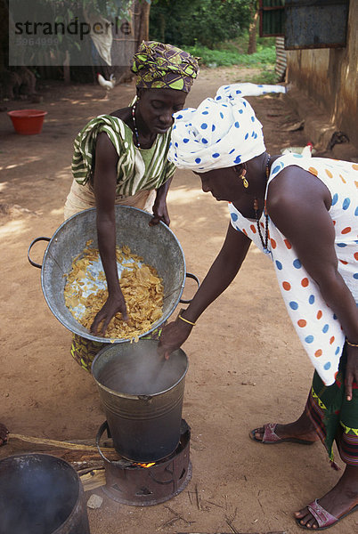 Zwei Frauen in traditioneller Kleidung  Kochen Suppe in einem Eimer über ein kleines Feuer im Freien  Gambia  Westafrika  Afrika