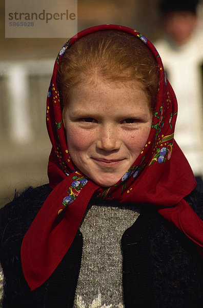 Kopf und Schultern Porträt von einem jungen rumänischen Mädchen mit roten Haaren tragen ein rotes Kopftuch  lächelnd und in die Kamera schaut  in Bottiza Dorf  Rumänien  Europa