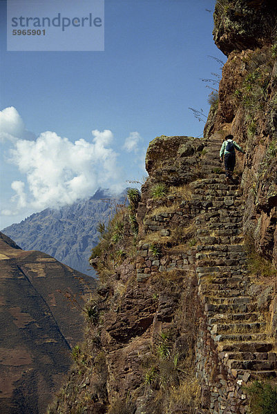 Ein Spaziergänger klettert die Schritte auf einem schmalen Pfad entlang dem Rand einer Klippe auf einer Inka-Stätte in der Urubamba-Tal  Pisac  Peru  Südamerika