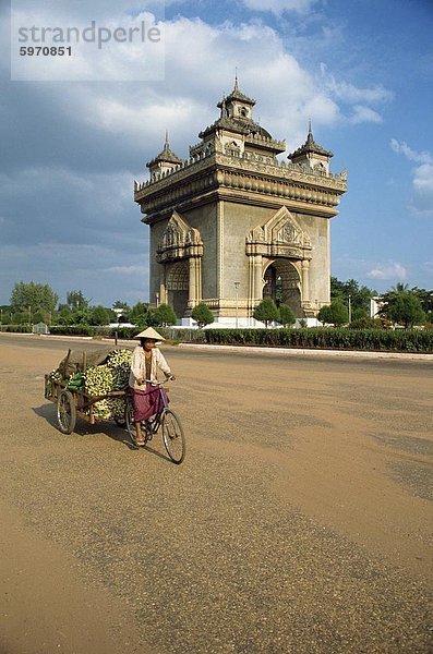 Frau auf einem Fahrrad mit Anhänger fährt vorbei an das Anousavari-Denkmal in Vientiane  Laos  Indochina  Südostasien  Asien