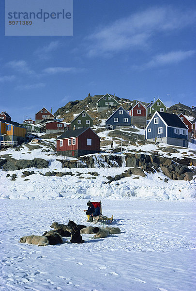 Huskies und Schlitten im Schnee  mit Häusern jenseits auf Angmagssalik in Grönland  Polarregionen