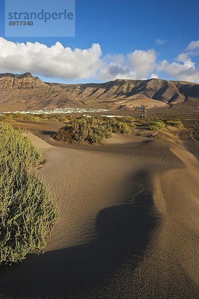 Vulkanische Felsen steigen bis 600 m über Wüstenlandschaft in der Nähe von Famara  mit seiner Entwicklung Flachbau Bungalow im Nordwesten der Insel  Famara  Lanzarote  Kanarische Inseln  Spanien  Atlantik  Europa