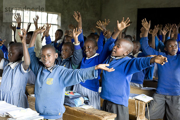 Schüler im Klassenzimmer  bietet traditionelle Kikuyu Begrüßung durch Hände winken  als ob Blumen  Karunga Primary School  Rift Valley in Kenia  Ostafrika  Afrika anbieten