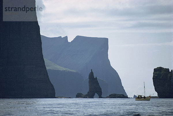 Kleines Fischerboot vor eine hoch aufragenden Felsen-Küste  Färöer  Dänemark  Atlantik  Europa