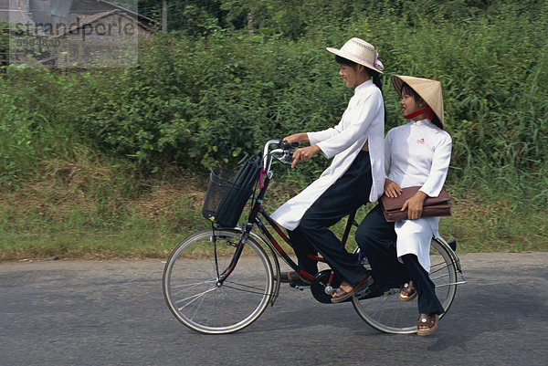 Zwei Schulmädchen in traditionellen Ao Dai auf einem Fahrrad in der Mekong-Delta-Region südlich von Ho-Chi-Minh-Stadt in Vietnam  Indochina  Südostasien  Asien