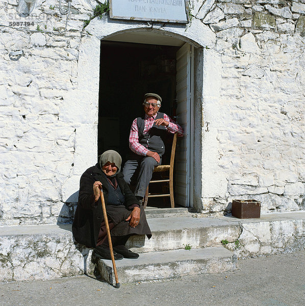 Alter Mann mit Brille  sitzt auf einem Stuhl und eine alte Frau mit einem Stock sitzt auf einen Schritt in einem Dorf in Griechenland  Europa