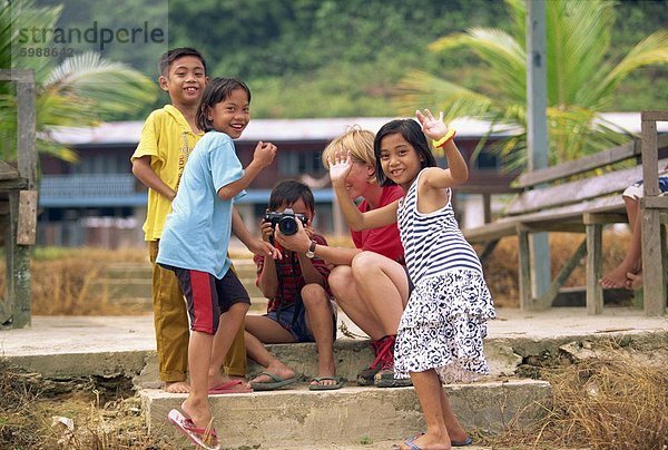 Eine Gruppe von Iban Dayak Kindern mit einem touristischen und Kamera außerhalb ihrer Langhaus auf dem Rajang River in der Nähe von Kapit Sarawak  Nordwest Borneo  Malaysia  Südostasien  Asien