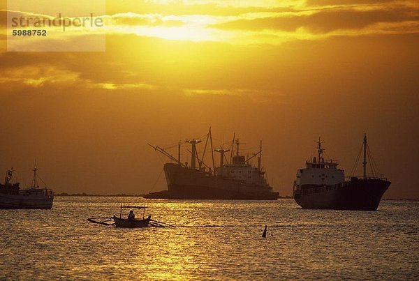 Frachtschiffe und Auslegerkanu in Manila Bay bei Sonnenuntergang  in den Philippinen  Südostasien  Asien