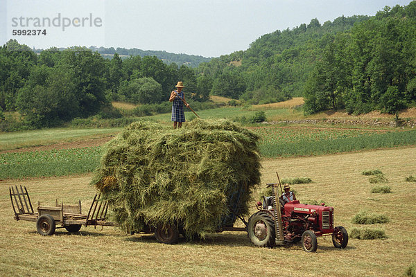 Landwirtschaft-Paar mit Traktor und volle Anhänger während der Heuernte in einem Feld nahe Lalbenque  Lot  Midi-Pyrenees  Frankreich  Europa